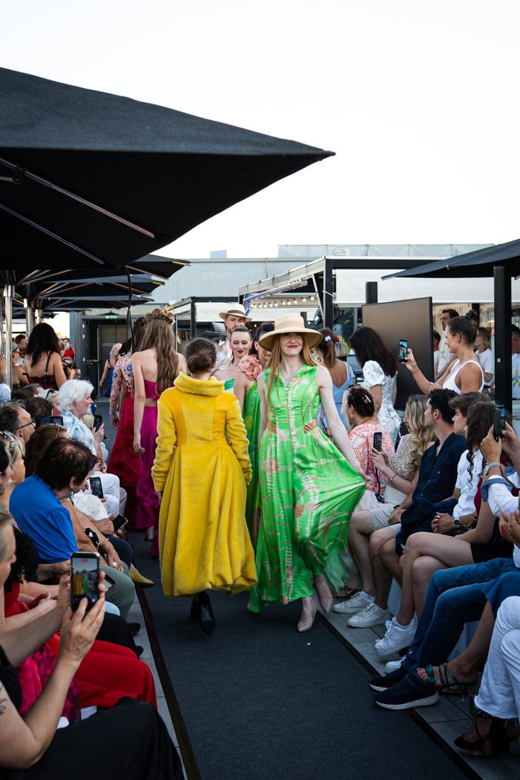 Modenschau auf einer Dachterrasse: Models in farbigen Kleidern laufen zwischen den Zuschauerreihen