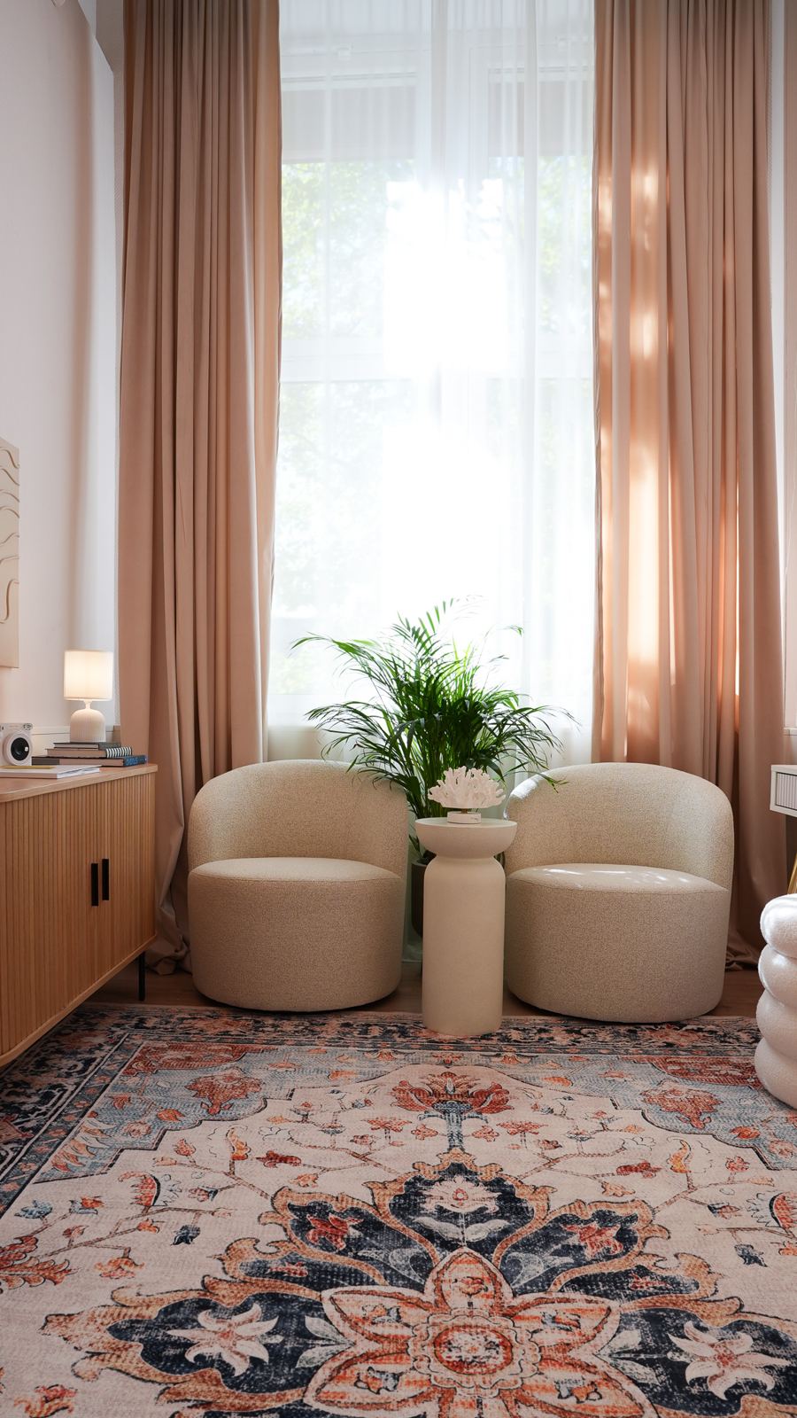 Wartebereich mit zwei Bouclé-Sesseln vor einem hohen Fenster mit rosé Vorhängen und Orientteppich