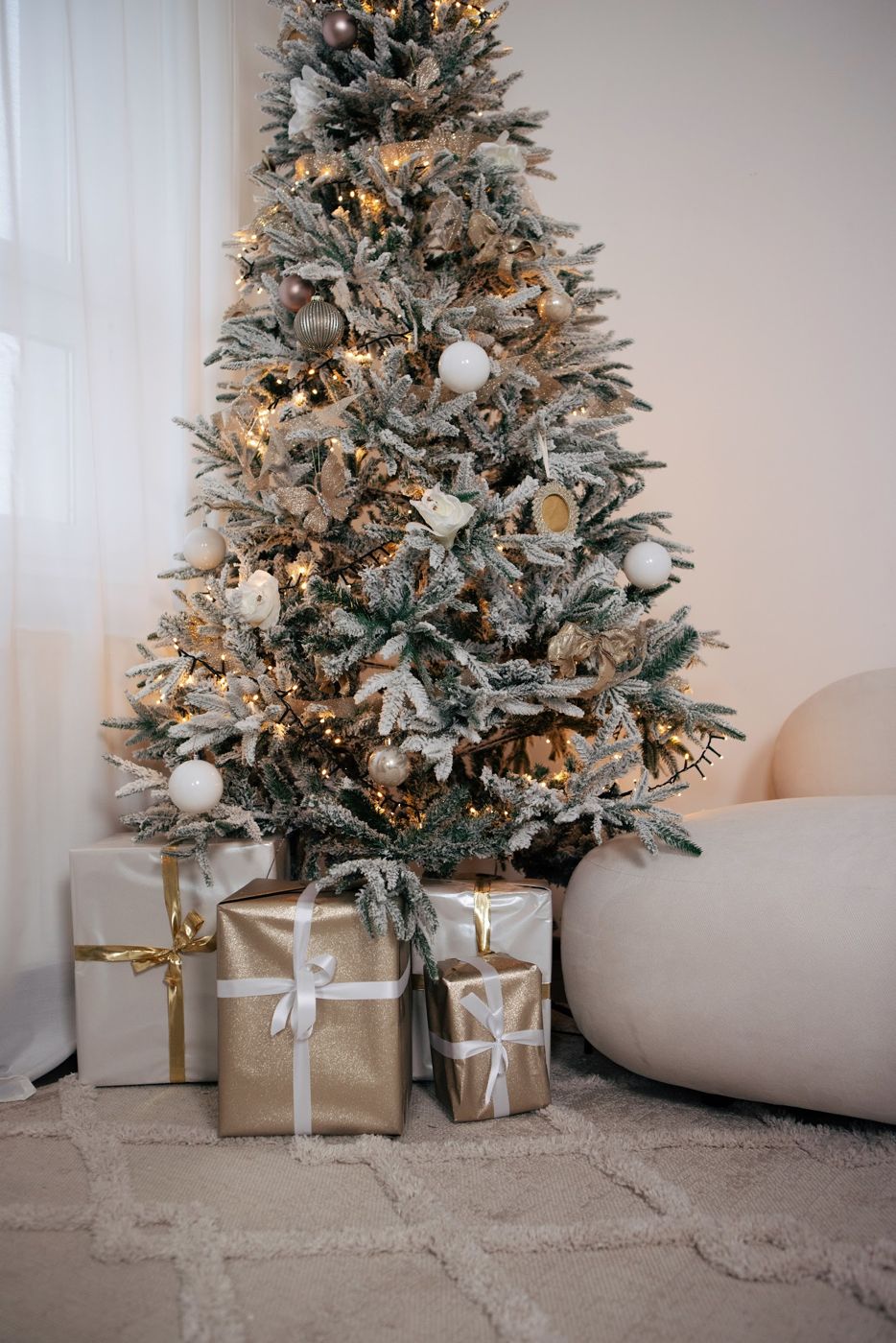 Verschneiter Weihnachtsbaum mit Lichterkette und Geschenken in Gold und Weiß