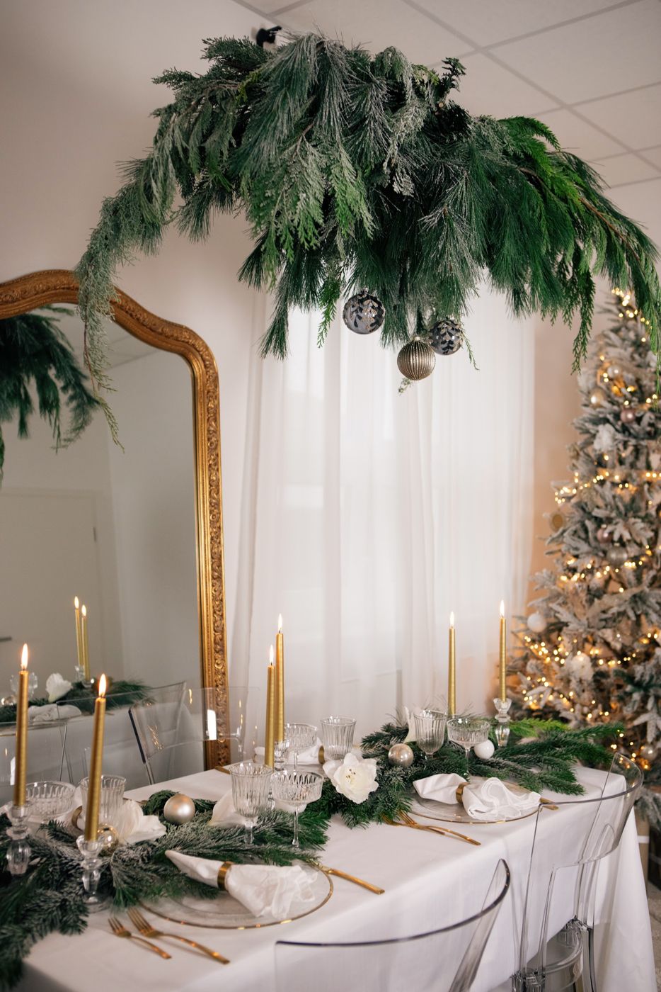 Festlich gedeckte Tafel mit goldenen Kerzen, Tannengirlande, Barockspiegel und verschneitem Weihnachtsbaum im Studio
